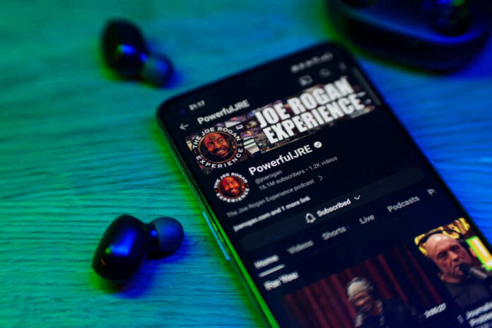 2432183549 Smartphone displaying podcast with wireless earbuds nearby.