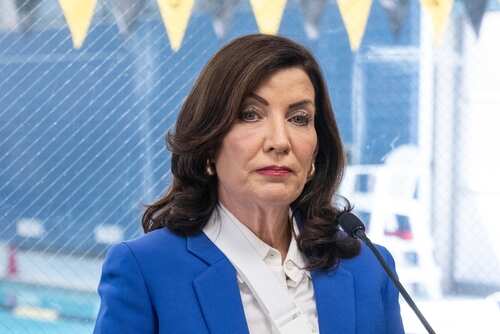 shutterstock_2409036021.jpg A woman in a blue blazer speaking at a podium with a microphone