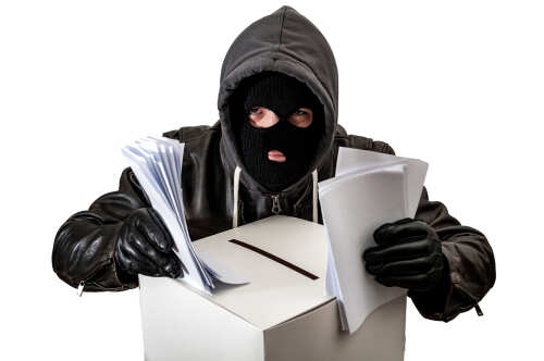 shutterstock_1057742687.jpg A masked individual in a hoodie stealing papers from a ballot box
