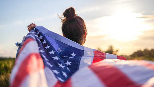 Person holding an American flag against a sunset backdrop