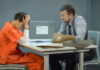 A detective interrogating a prisoner in an orange jumpsuit at a table