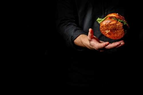 A chef's hand tossing a burger against a black background