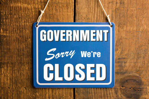 A blue sign stating 'GOVERNMENT Sorry We're CLOSED' hanging on a wooden surface