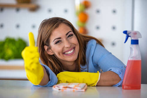Smiling woman in yellow gloves giving a thumbs up in a kitchen