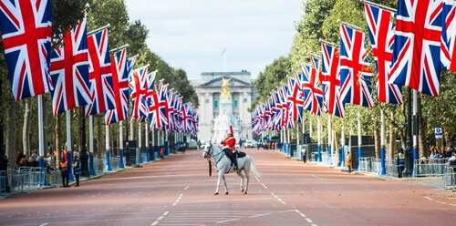 A horse rider in a red uniform stands on a road lined with British flags leading to Buckingham Palace
