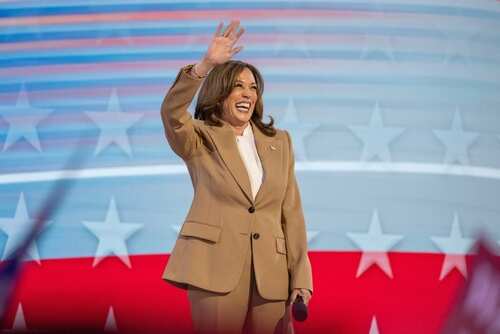 A smiling female politician waves to the audience at a political event