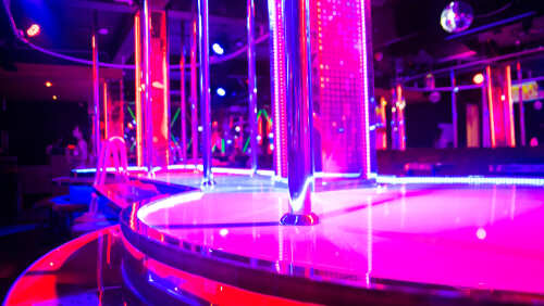 Interior of a nightclub with colorful neon lights and a dance pole