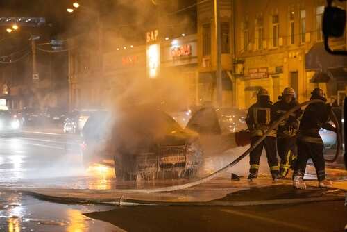 Firefighters extinguishing a car fire on a city street at night