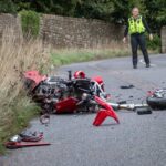 A damaged motorcycle on the side of the road with police officers nearby