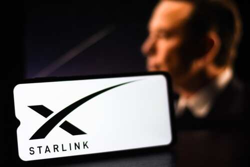 shutterstock_2442885775.jpg A smartphone displaying the Starlink logo with a blurred figure in the background