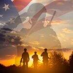Silhouetted soldiers against a backdrop of the American flag and a sunset
