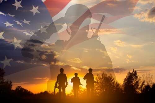 Silhouetted soldiers against a backdrop of the American flag and a sunset