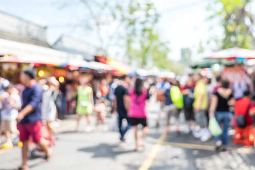 Crowd of people at a bustling outdoor market with colorful stalls