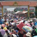 Mass Evacuation Chaos: Disaster Inevitable! A large crowd of people carrying various goods through a market entrance