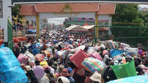 A large crowd of people carrying various goods through a market entrance