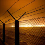 Barbed wire fence illuminated by distant industrial lights in a foggy night
