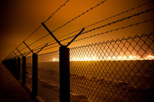 Barbed wire fence illuminated by distant industrial lights in a foggy night
