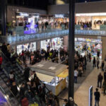 A busy shopping mall with escalators and numerous shoppers