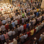 A large group of men participating in a prayer service inside a mosque