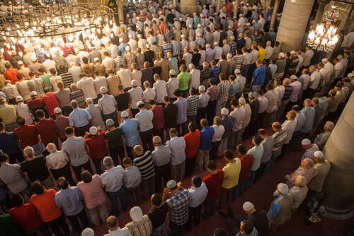 A large group of men participating in a prayer service inside a mosque
