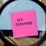 A magnifying glass focusing on a pink sticky note that reads 'SEX OFFENDER'