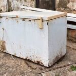 An old, rusty freezer sitting outdoors on a concrete surface