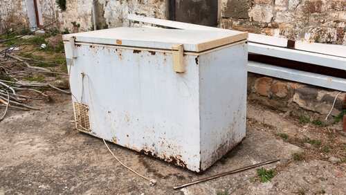 An old, rusty freezer sitting outdoors on a concrete surface