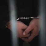 Hands in handcuffs behind bars