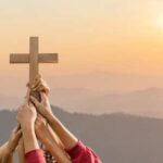 Hands holding a wooden cross against a sunrise backdrop