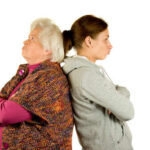 An older woman and a younger woman standing back to back with displeased expressions