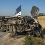 An overturned van on the side of the road with a person inspecting it