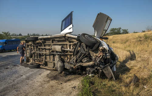 An overturned van on the side of the road with a person inspecting it
