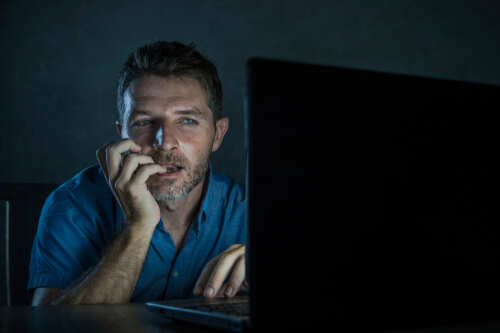 Man sitting in front of a laptop with a focused expression in a dimly lit room