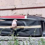 A hand emerging from an open suitcase on a concrete surface