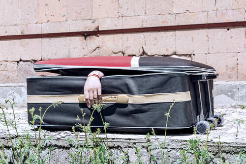 shutterstock_1736603390.jpg A hand emerging from an open suitcase on a concrete surface