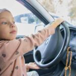 A young girl playfully pretending to drive a car