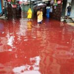 People walking through a flooded street with reddish water