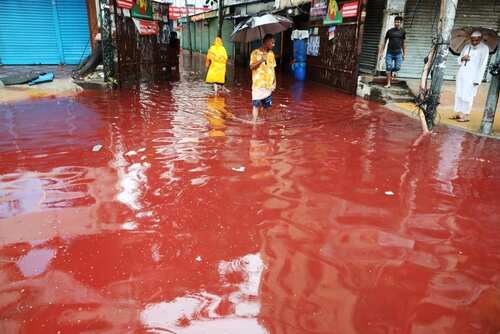 People walking through a flooded street with reddish water