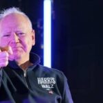 A man in a dark sweater pointing directly at the camera with a confident expression