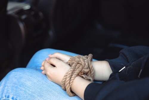 Hands bound with rope resting on a lap
