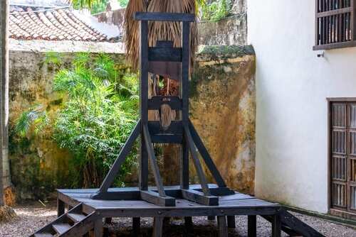 A wooden guillotine displayed in an outdoor area surrounded by greenery
