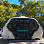An autonomous shuttle vehicle parked on a city street surrounded by trees