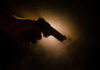 Silhouette of a hand holding a gun against a dark background with dramatic lighting