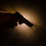 Silhouette of a hand holding a gun against a dark background with dramatic lighting