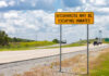 Statewide PANIC: Dangerous Inmates on the Loose A warning sign on a highway indicating potential hitchhikers may be escaping inmates