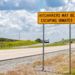 A warning sign on a highway indicating potential hitchhikers may be escaping inmates