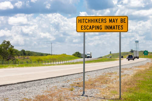 A warning sign on a highway indicating potential hitchhikers may be escaping inmates
