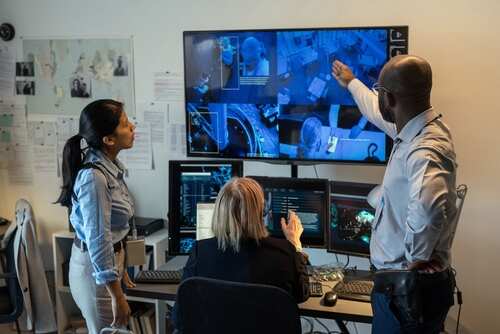 Three professionals analyzing security footage on multiple screens