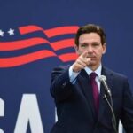 A man in a suit pointing while speaking at a podium with a microphone