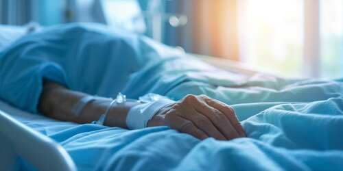 A patient's hand resting on a hospital bed with an IV line attached
